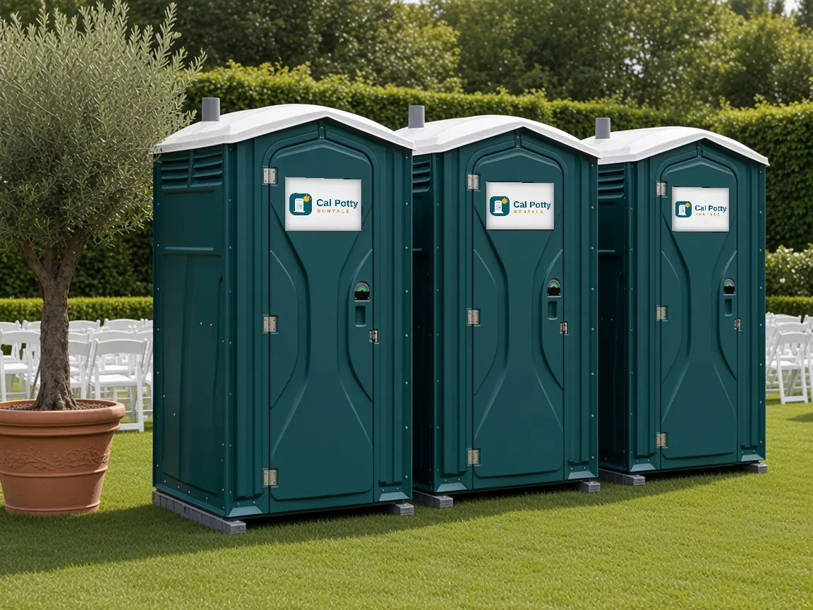 Three teal portable toilets on a lawn beside a potted olive tree and white chairs